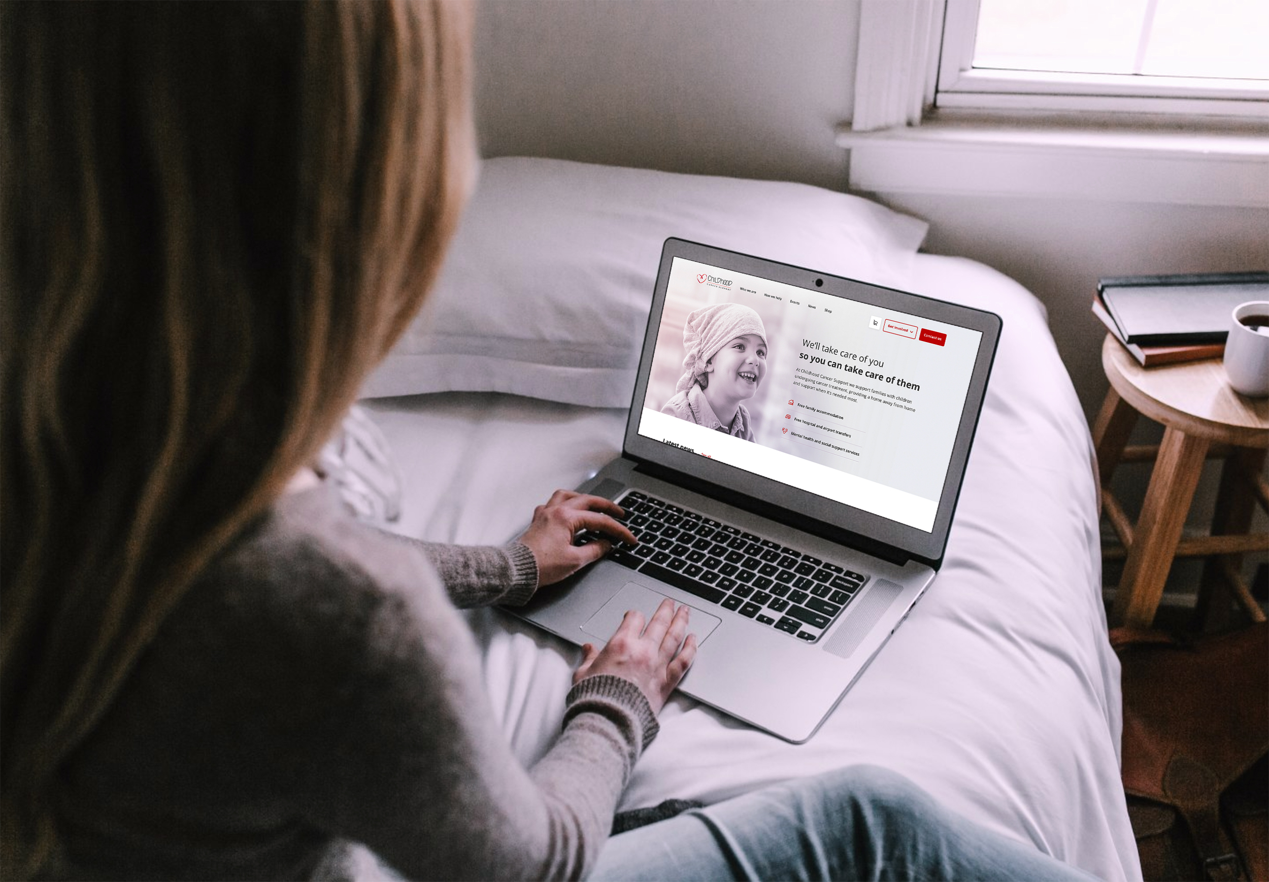 Woman in front of laptop mockup of Childhood Cancer Support homepage.